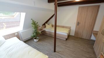 Een slaapkamer met een bed, een kleine zithoek, een potplant en een houten garderobe.