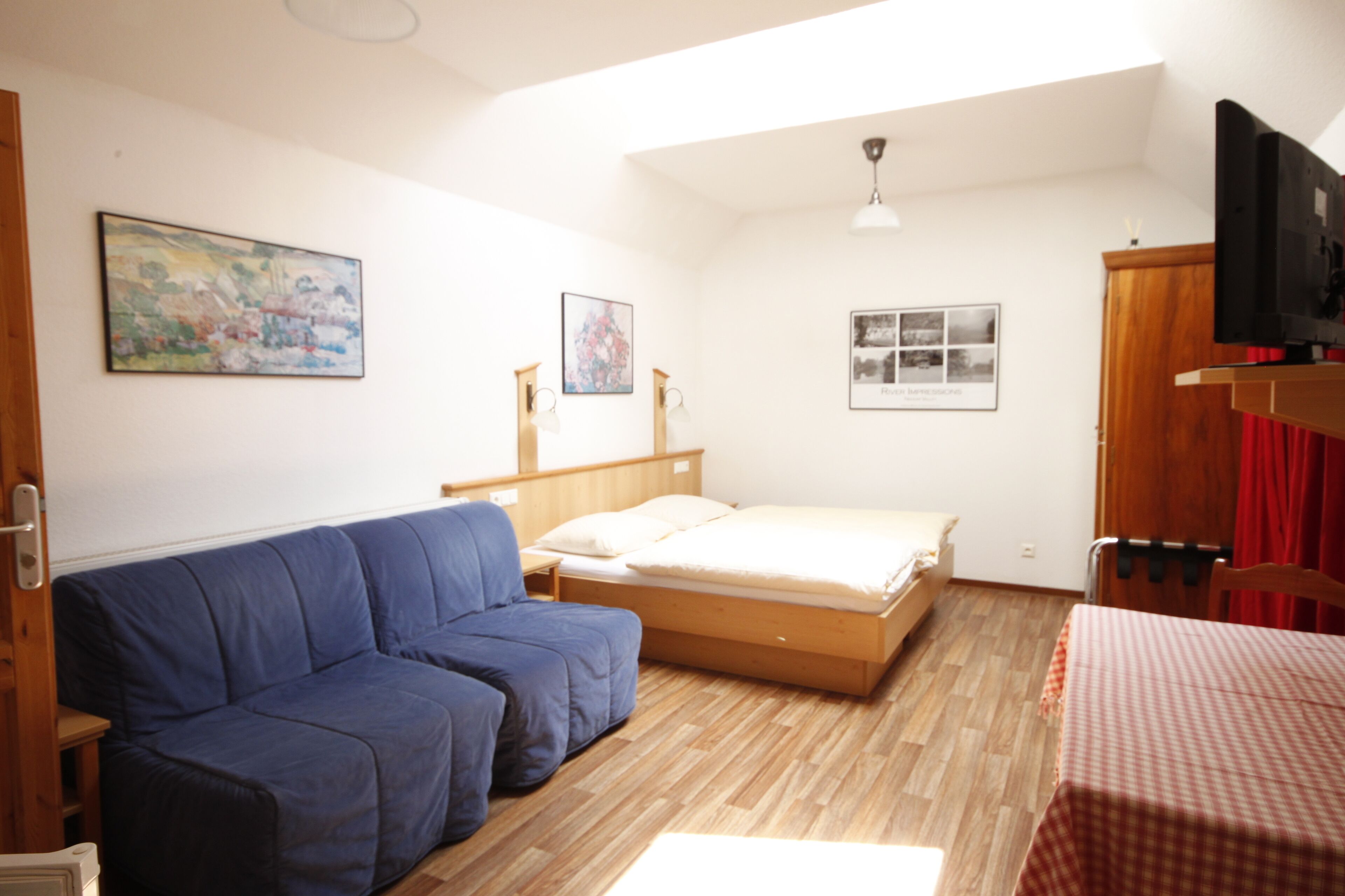 A room with a blue sofa, a wooden bed, a television, and a painting on the wall.