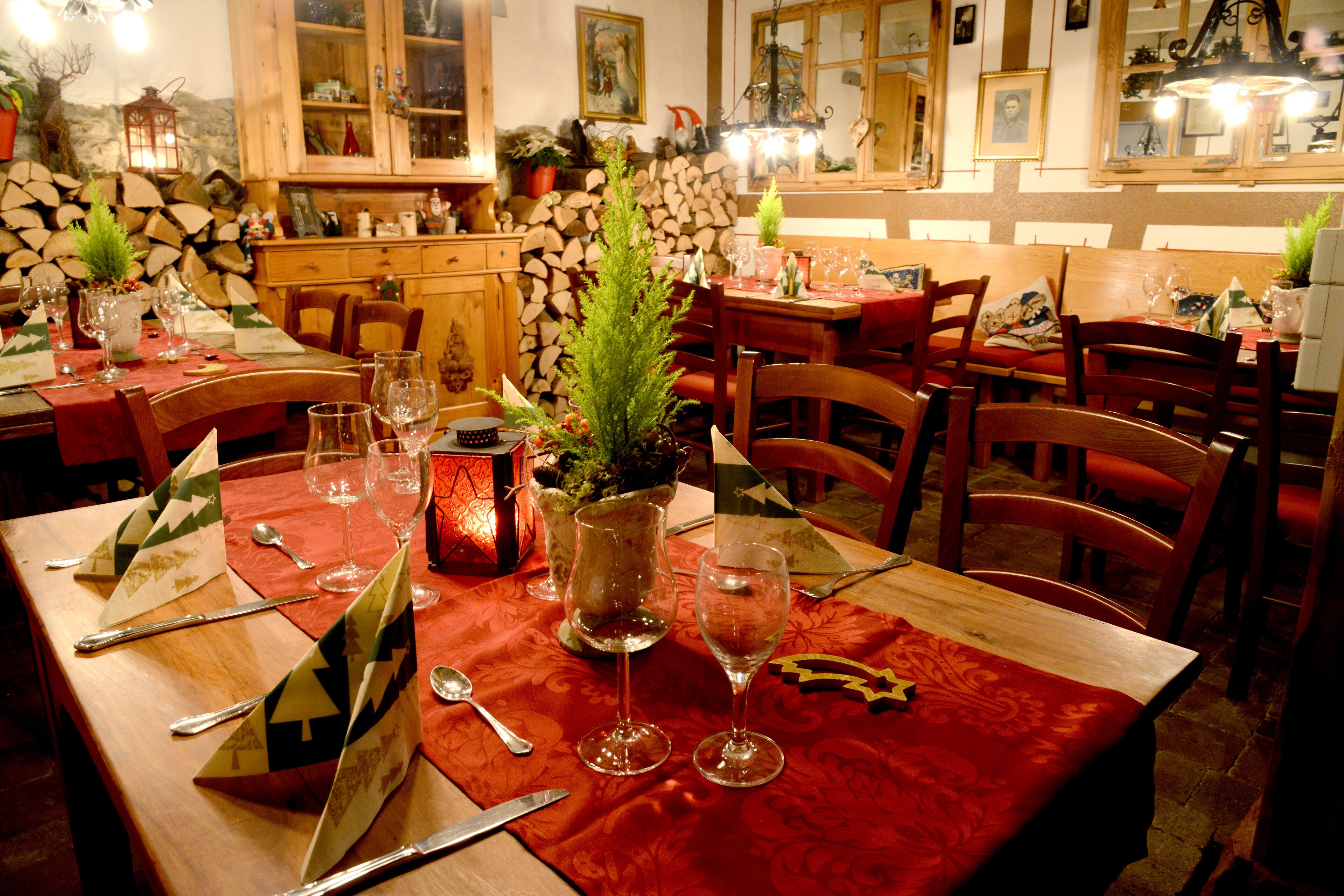 Un'area pranzo con tavoli di legno, tovaglie rosse e bicchieri da vino apparecchiati per un pasto.