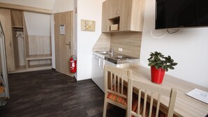 A compact kitchen with wooden cabinets, a built-in stove, and a single chair with a striped cushion. - Am Treidelpfad (Hassmersheim)
