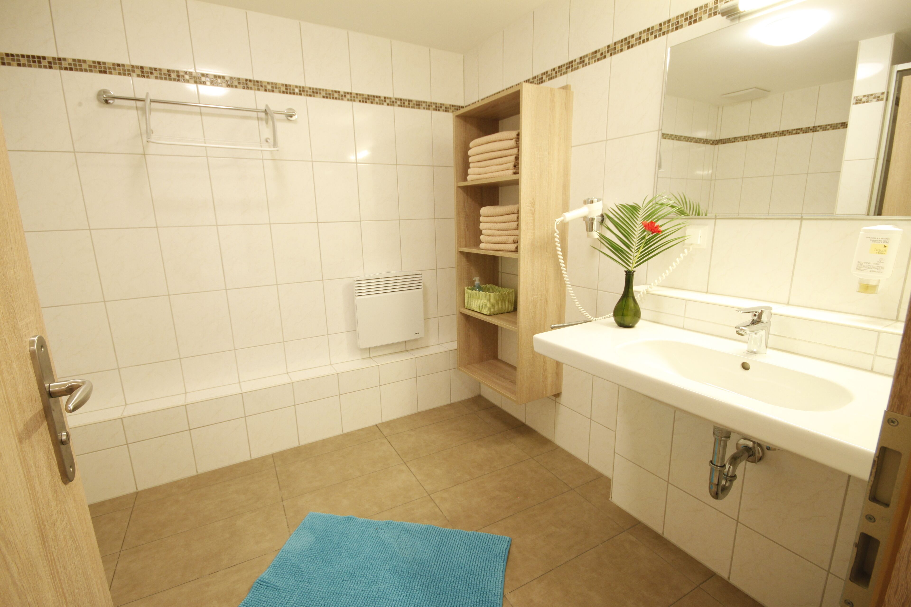 Un baño con lavamanos blanco, espejo y toallero.