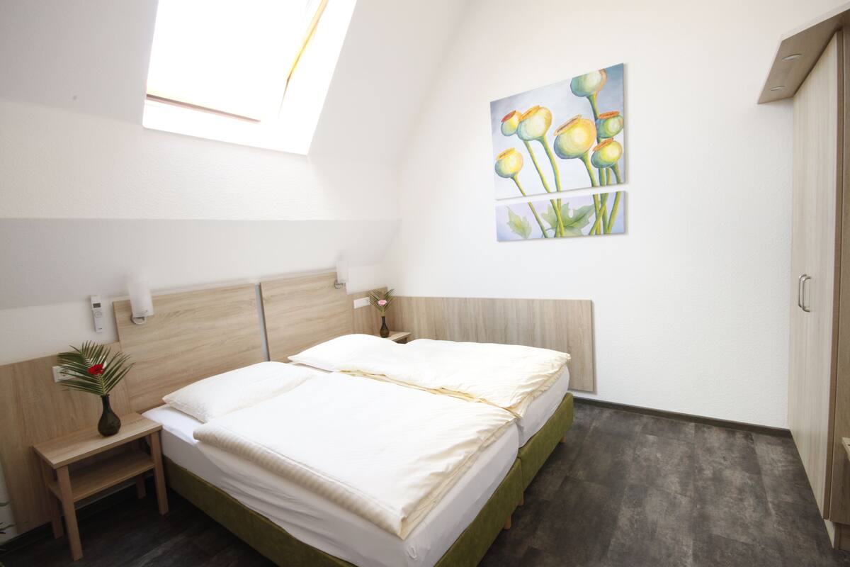 A bedroom with a bed, bedside tables, a nightstand, a painting, and a window.