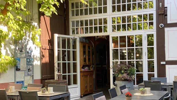 An outdoor dining area with tables and chairs, a large window with multiple panes, and a door leading to an interior space. - Am Treidelpfad (Hassmersheim)