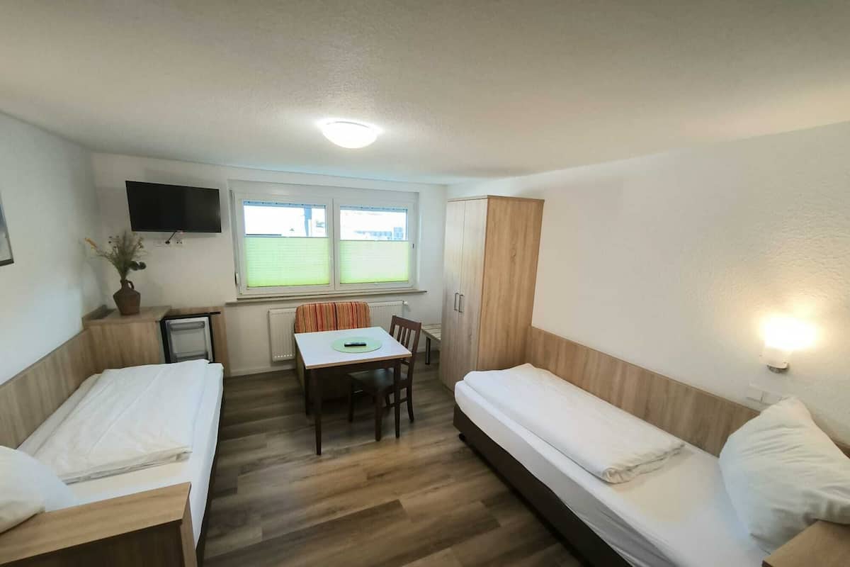 A small, well-lit room with a bed, a sofa, a table, and a TV.