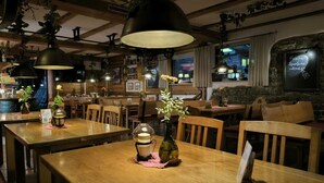 A cozy restaurant interior with wooden tables, hanging plants, and pendant lighting. - Am Treidelpfad (Hassmersheim)