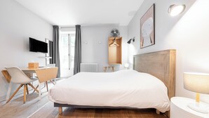 Une chambre d’hôtel moderne équipée d’un lit, d’un bureau, d’une chaise et d’un téléviseur fixé au mur.