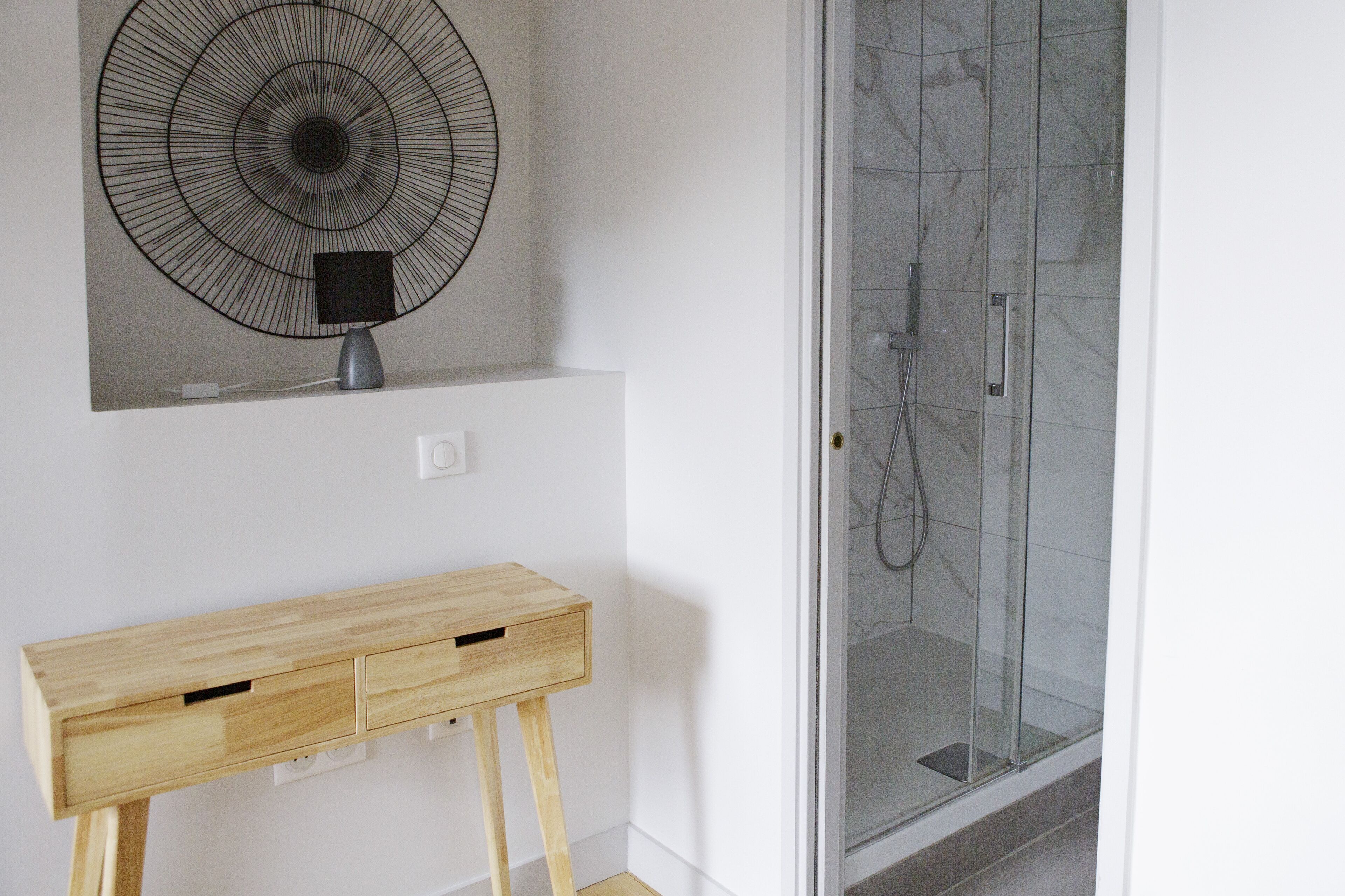 A bathroom with a glass shower enclosure, a wall-mounted fan, and a wooden console table.