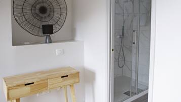 Un baño con cabina de ducha de vidrio, un ventilador de pared y un mueble consola de madera.