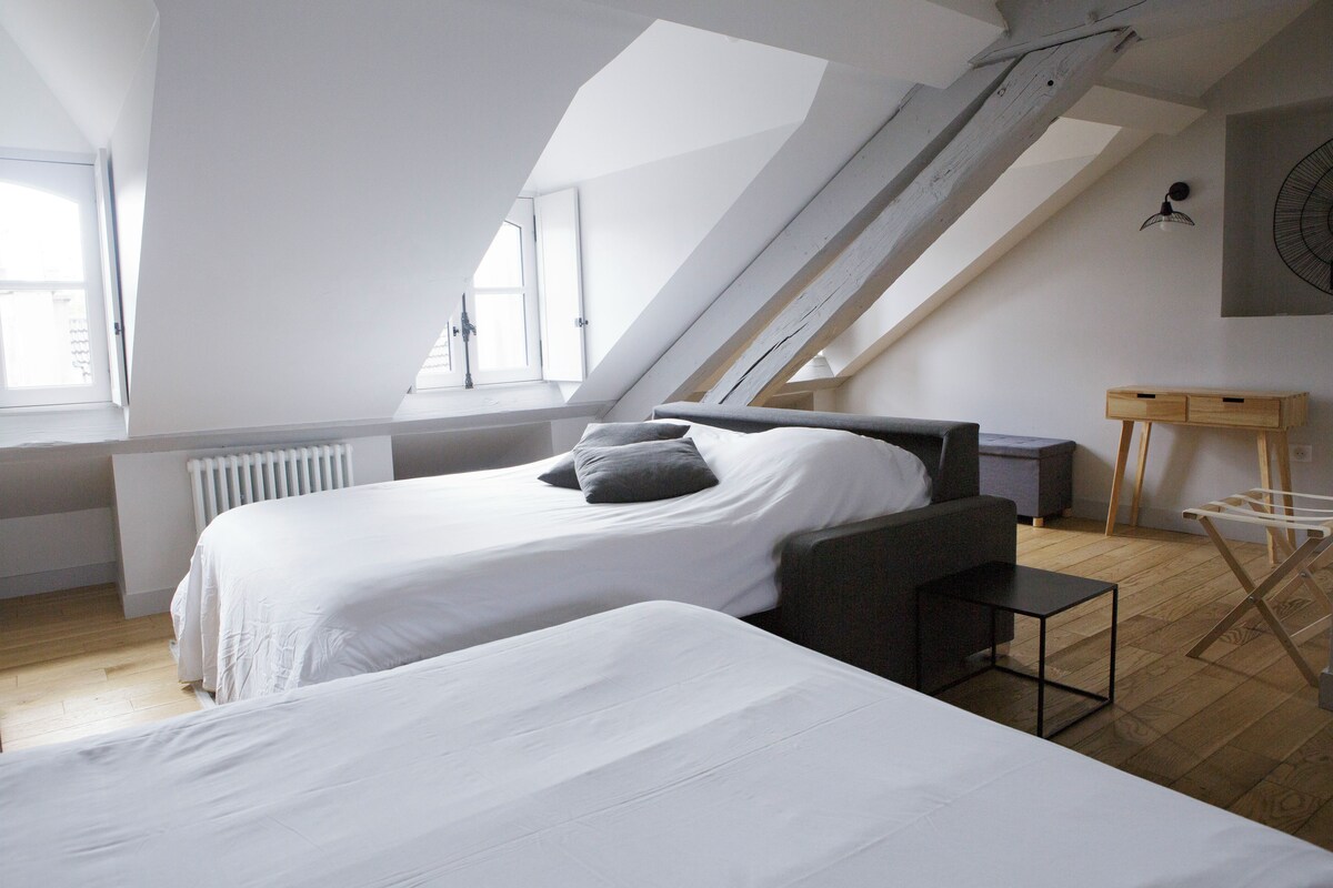 Et soveværelse med to senge, skråvæg, radiator, et lille bord og en vægmonteret ventilator.