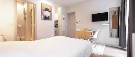 A hotel room with a large bed, a desk with a chair, a TV mounted on the wall, and a shower area.