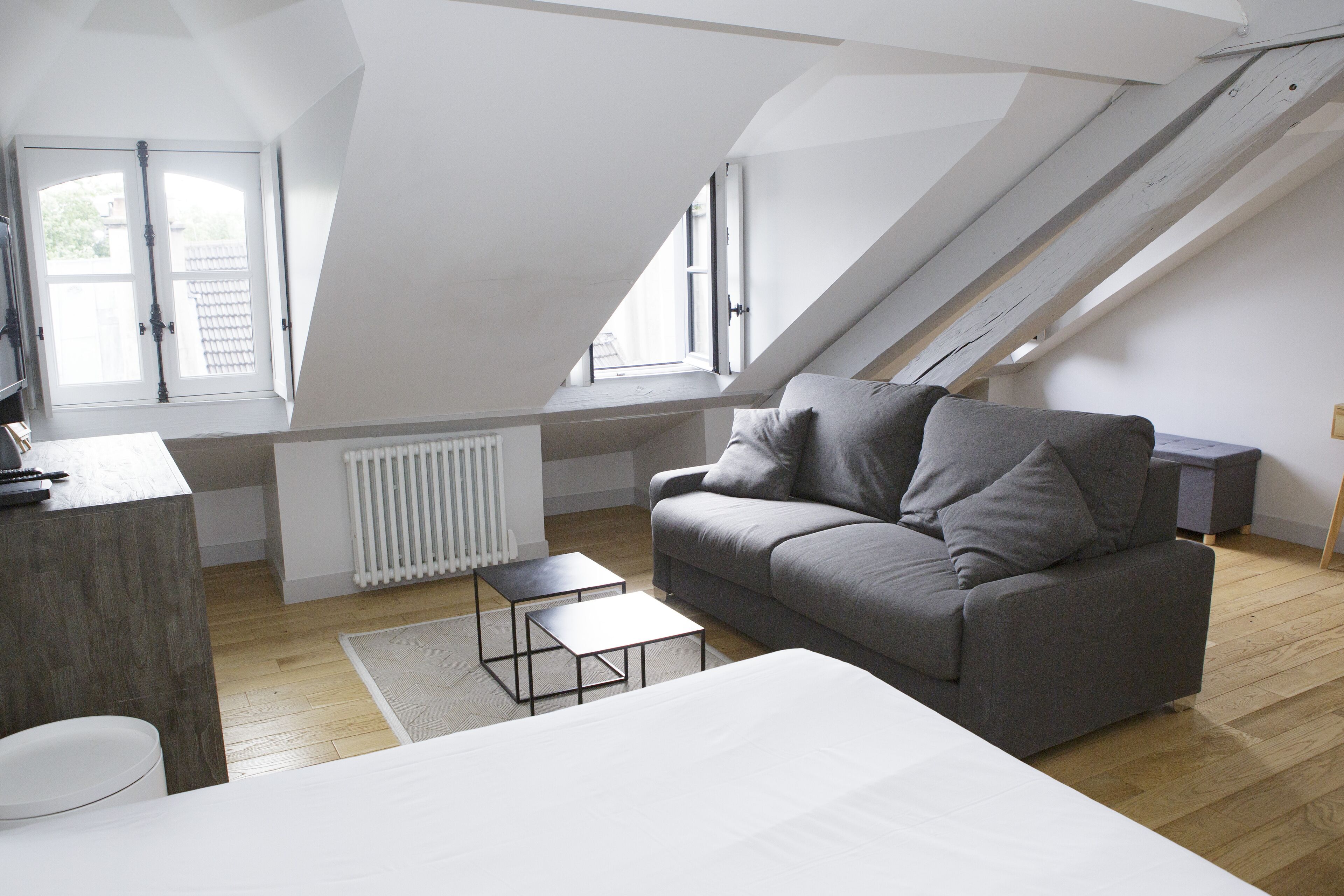 Une chambre de style loft moderne, avec un plafond en pente, un canapé gris, une petite table blanche et un radiateur.
