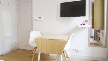Une petite pièce moderne avec une porte blanche, une chaise blanche, une petite table, un téléviseur fixé au mur et un panneau indiquant « Il est interdit de fumer ».