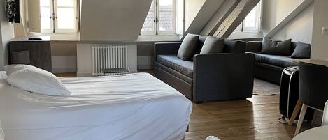 A modern loft bedroom with a large bed, a sofa, and a dining area.