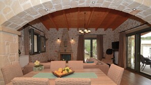 A dining area with a stone fireplace, wooden ceiling, and wicker furniture. - Villa Lobos (Zakynthos)