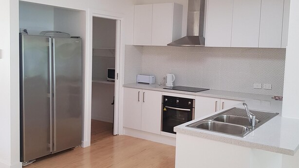 Una cocina moderna con armarios blancos, un refrigerador de acero inoxidable, horno empotrado y un lavamanos en la encimera.