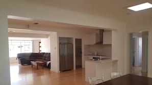Amplia sala de estar con una mesa de comedor de madera oscura, un sofá y una cocina que incluye un refrigerador y un microondas.