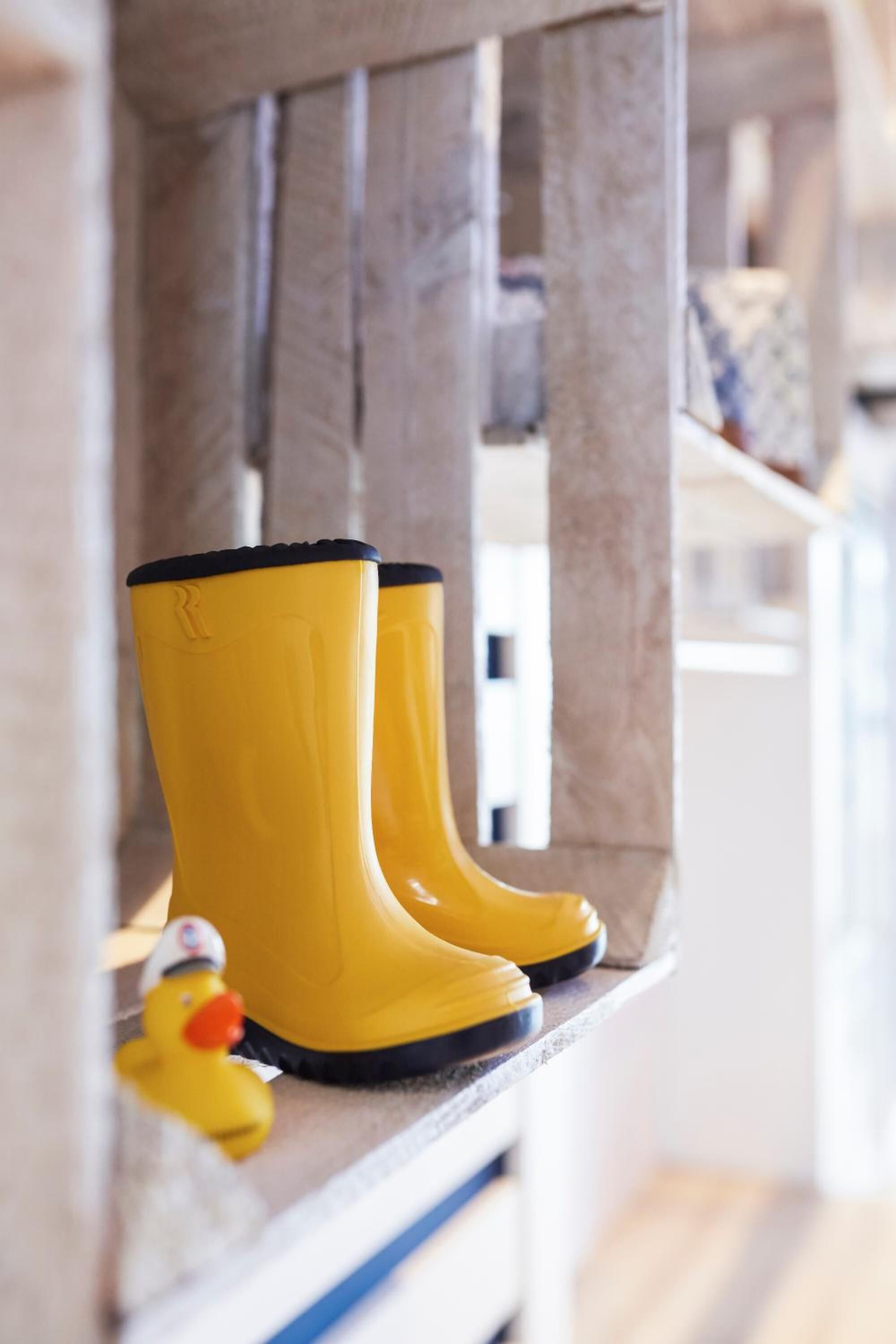 A pair of yellow rubber boots on a wooden shelf.