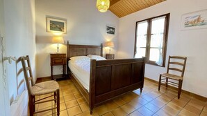 A bedroom with a wooden bed, two bedside lamps, a window with curtains, and a chair.