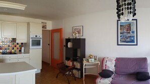 A compact living space with a kitchenette, a bookshelf, and a seating area with a purple sofa.