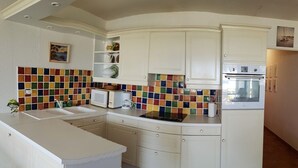 A compact kitchen with white cabinetry, a colorful backsplash, and a built-in oven.