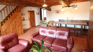 Una sala de estar acogedora con una escalera de madera, un comedor con un banco, y un sofá de cuero rojo.