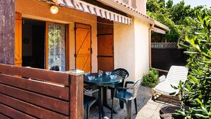 A building with a number '52' on the facade, a patio area with a table and chairs, and a wooden bench. - Air-conditioned 3-Room Pavilion with Terrace, Parking, and Wi-Fi - Sleeps 4 (Narbonne-Narbonne Plage-Narbonne Plage)