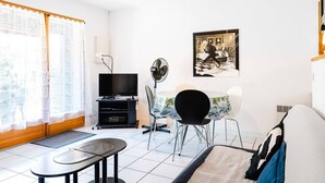 A modern living room with a TV, fan, and artwork on the wall. - Air-conditioned 3-Room Pavilion with Terrace, Parking, and Wi-Fi - Sleeps 4 (Narbonne-Narbonne Plage-Narbonne Plage)