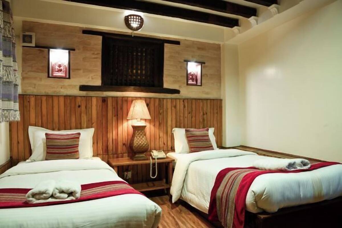 A hotel room with two beds, wooden paneling, a wall-mounted lamp, and a telephone on a bedside table.