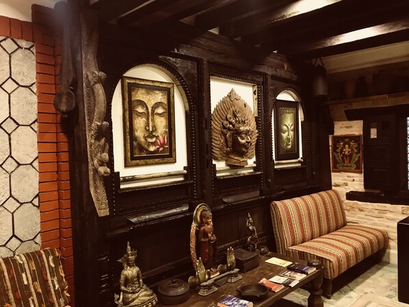 A room with a sofa, a table with books, and framed Buddha statues. - Nepal Pavilion Inn (Kathmandu)
