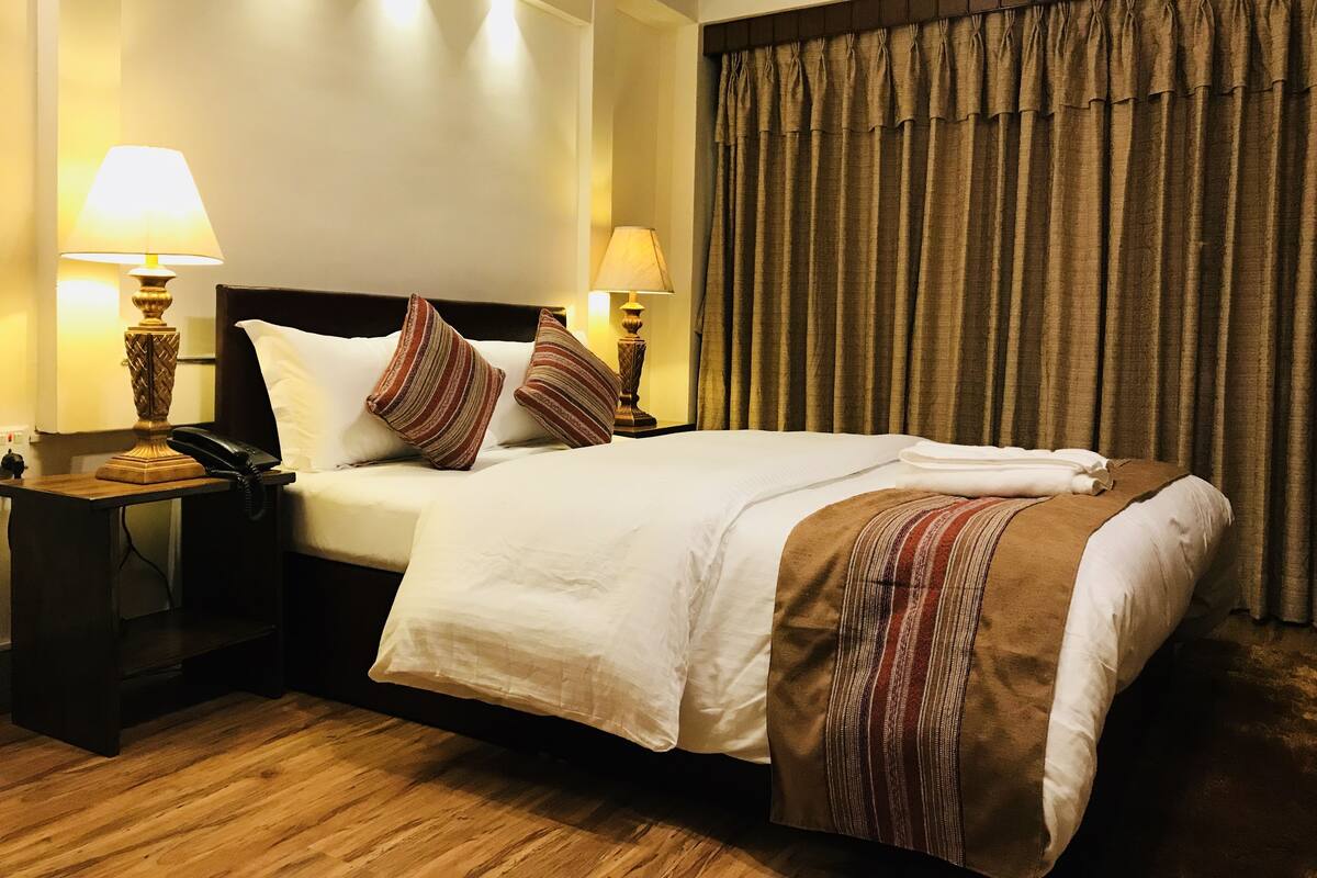 A hotel room with a large bed, two bedside lamps, a telephone, and a curtain.