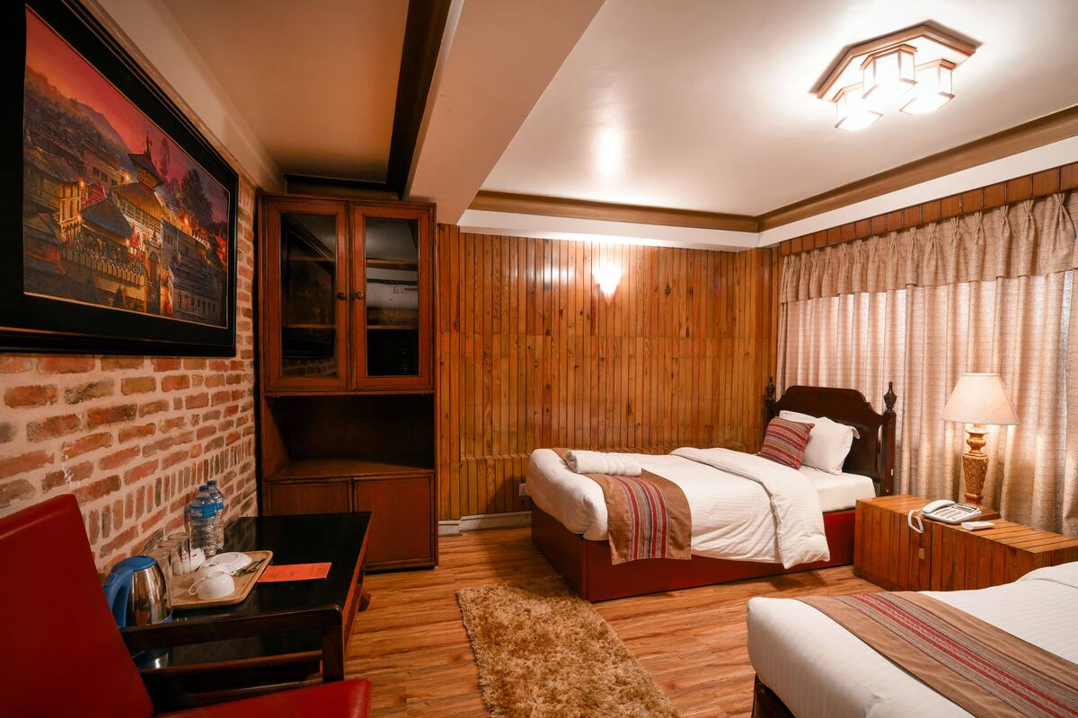 A hotel room with two beds, wooden paneling, a painting, a desk with a chair, and a nightstand with a lamp.