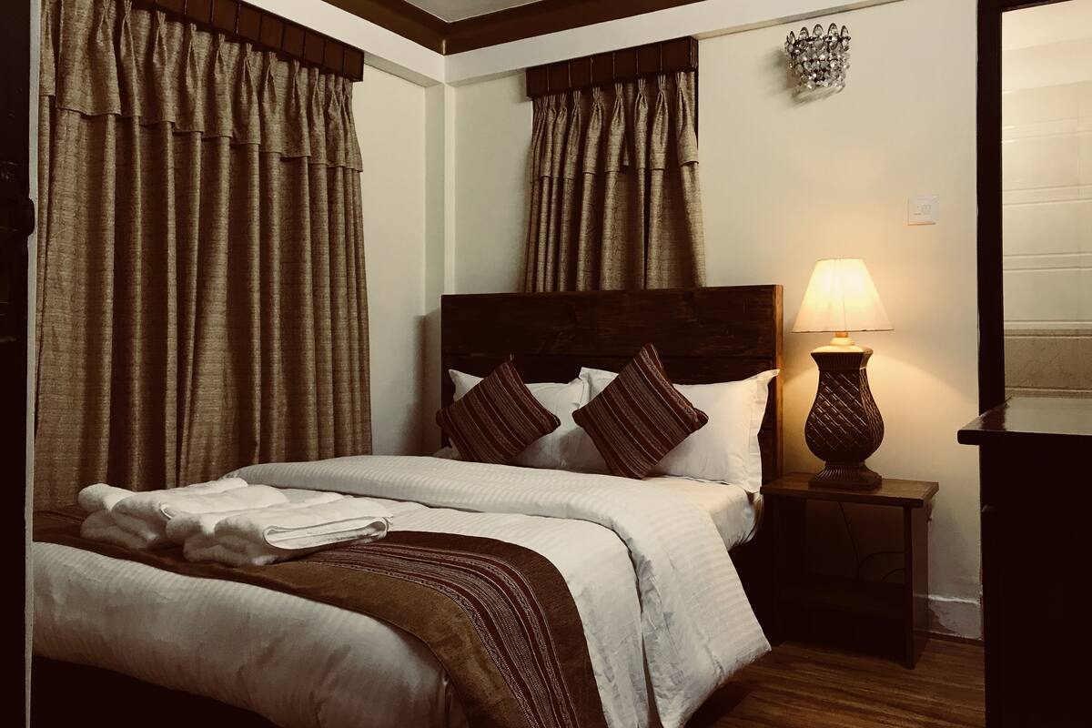 A neatly made bed with a wooden headboard, a bedside lamp, and curtains on a window.