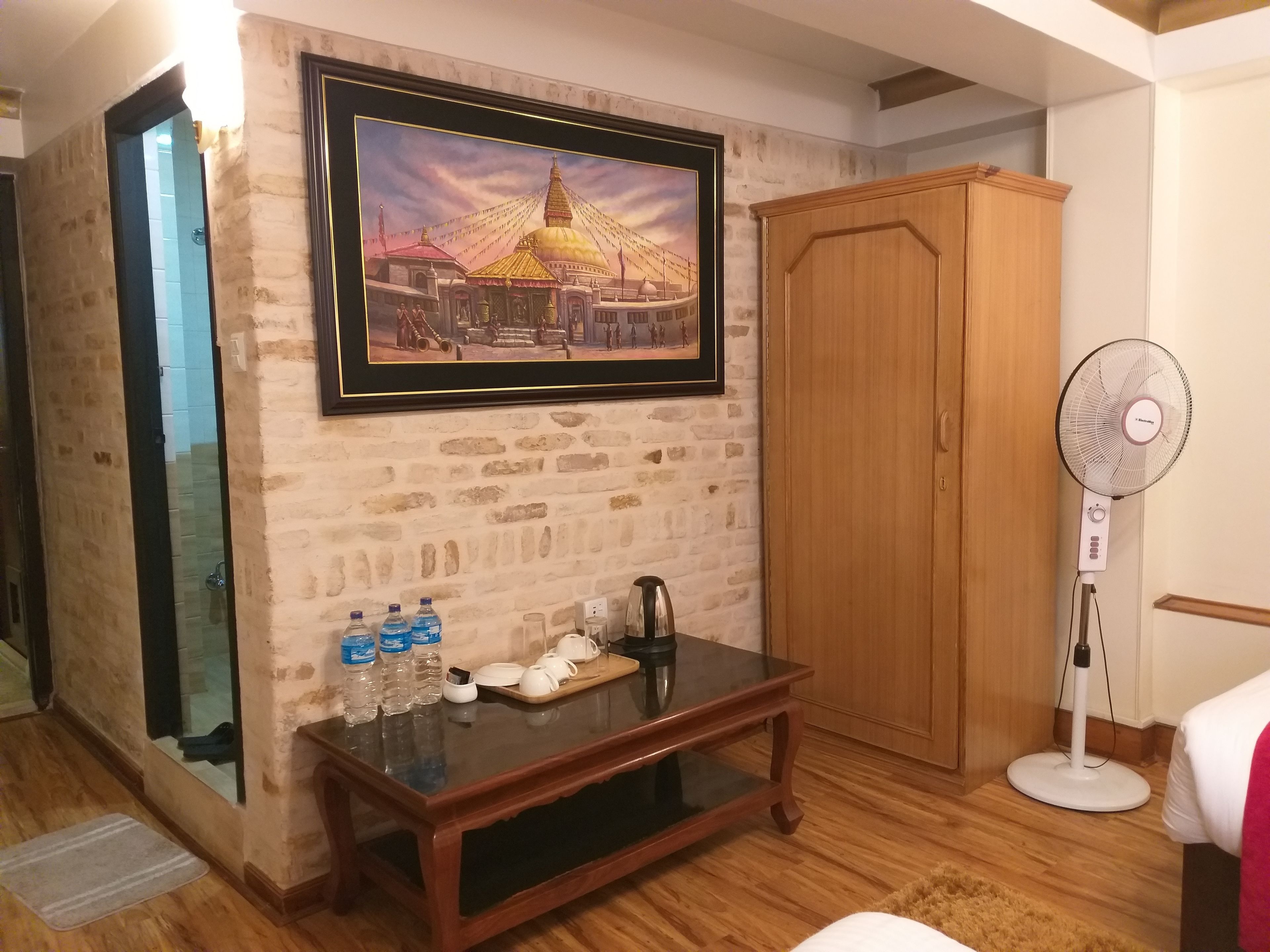A room with a stone wall, a wooden cabinet, a glass table with water bottles, a coffee maker, and a framed picture of a building.