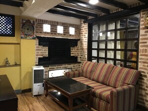 A cozy living room with a patterned sofa, a small table, a decorative wall piece, and a window with a view. - Nepal Pavilion Inn (Kathmandu)