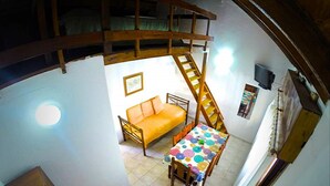 Una habitación compacta con una cama, una mesa con mantel colorido, una escalera de madera y un pequeño sofá.