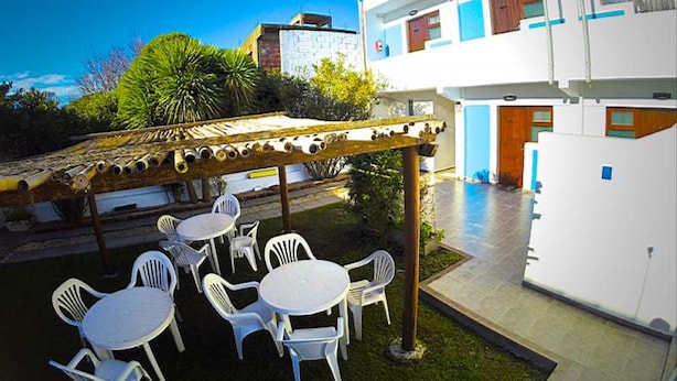Un patio con mobiliario exterior, una pérgola y un edificio de fachada azul y blanca.