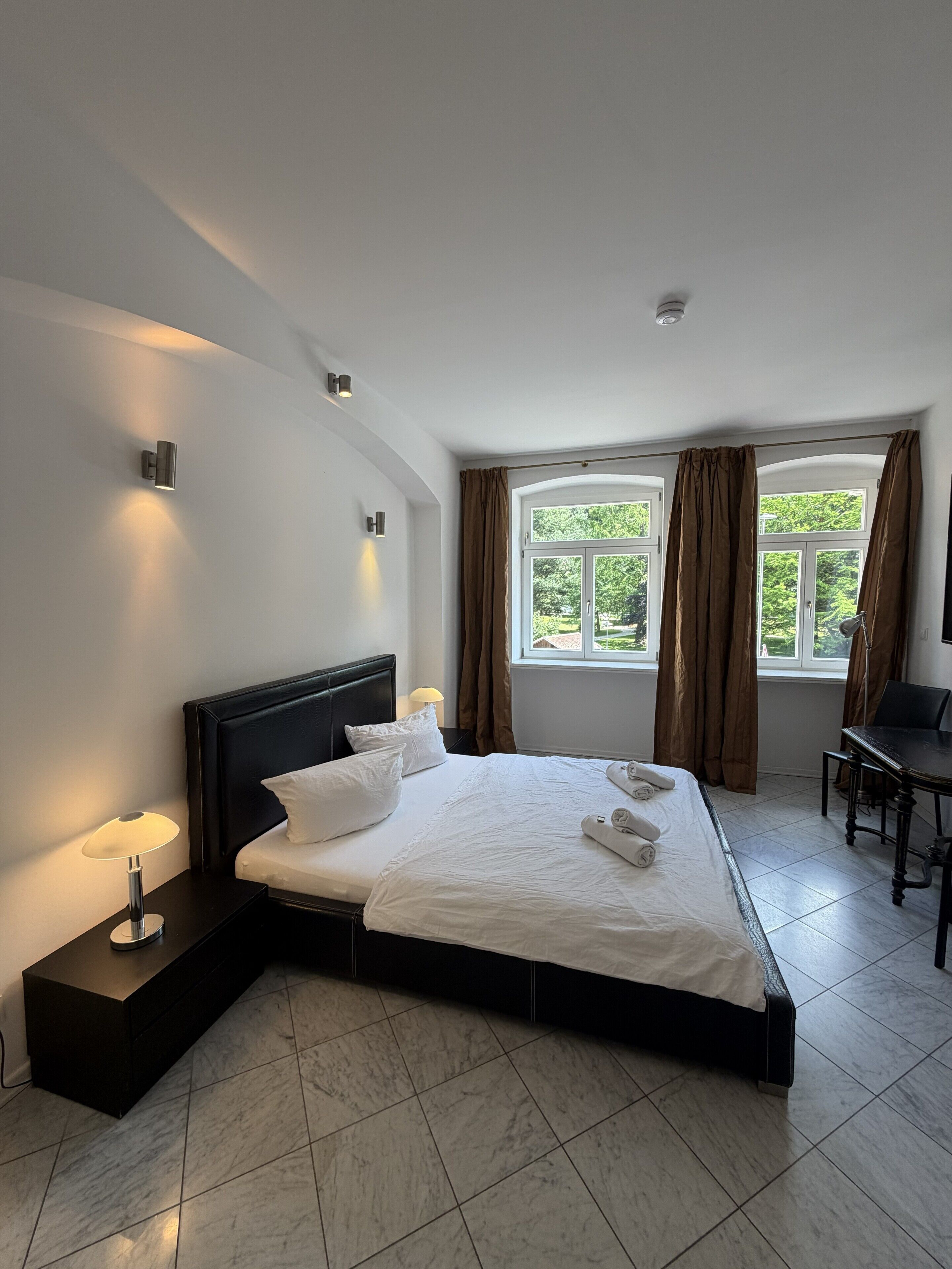 Une chambre d’hôtel moderne avec un grand lit, des lampes de chevet, un bureau et une fenêtre avec des rideaux.