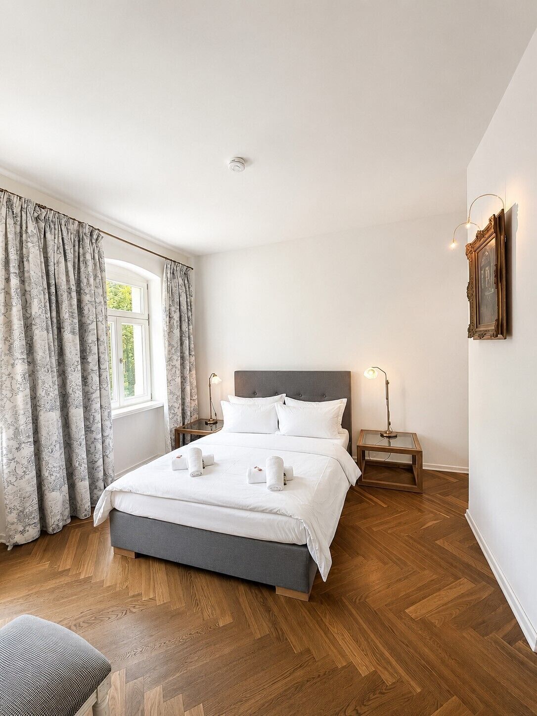 A neatly arranged bedroom with a bed, bedside tables, a chair, and a window with curtains.