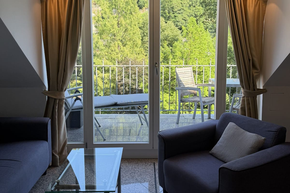 Een kamer met een glazen tafel, een bank en uitzicht op een balkon met stoelen.