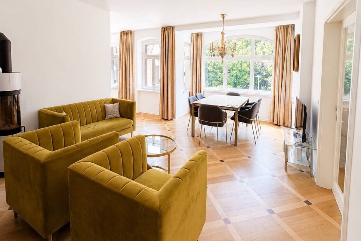 Een moderne woonkamer met een zithoek, een eettafel met stoelen, een open haard en grote ramen met gordijnen.