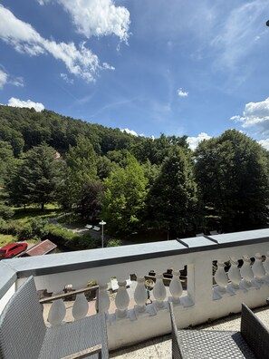 Un balcó amb vista a una vessant de muntanya verda i un cotxe vermell aparcat a sota.