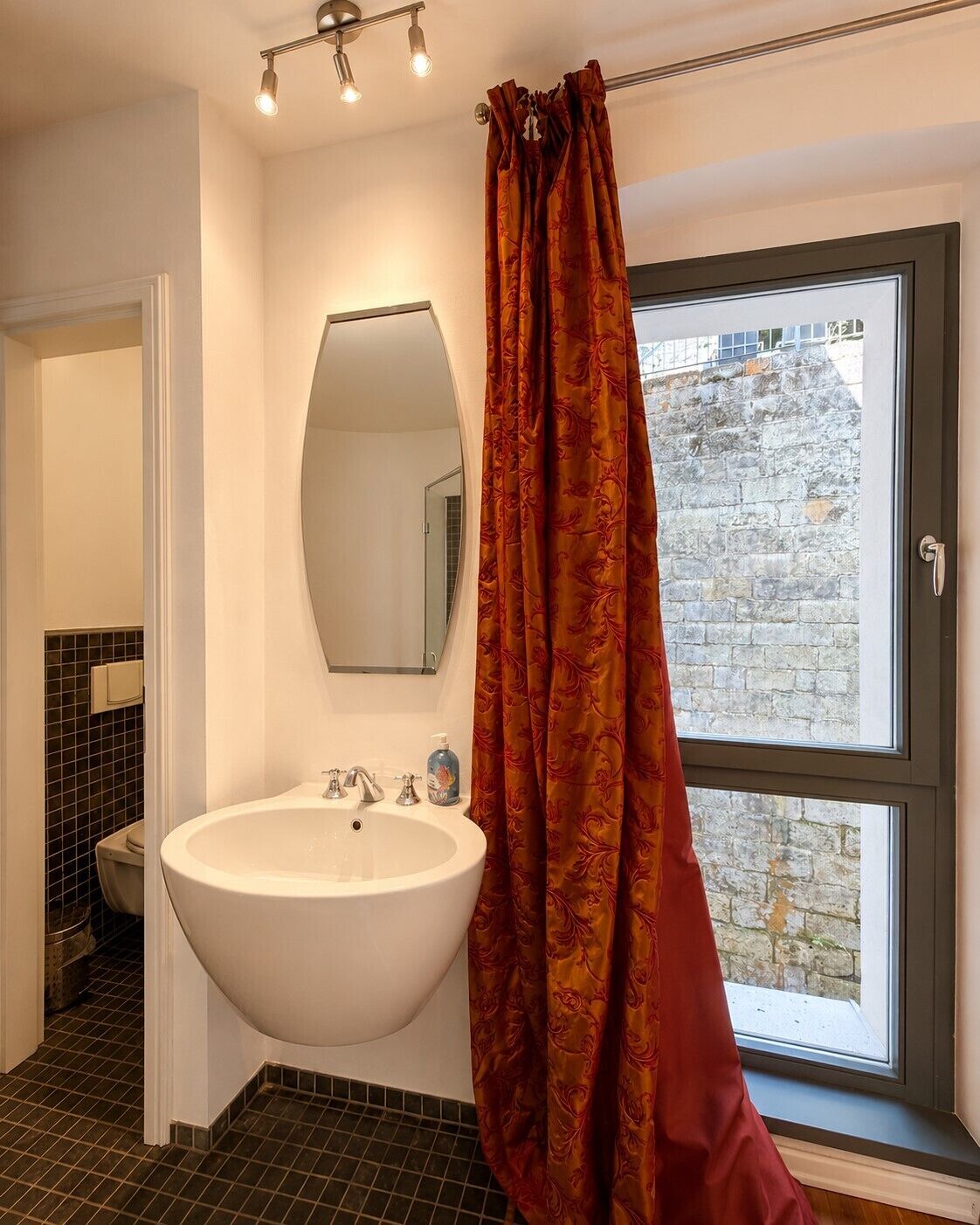 Un baño con un lavamanos grande de color blanco, un espejo y una ventana que da a una pared de piedra.