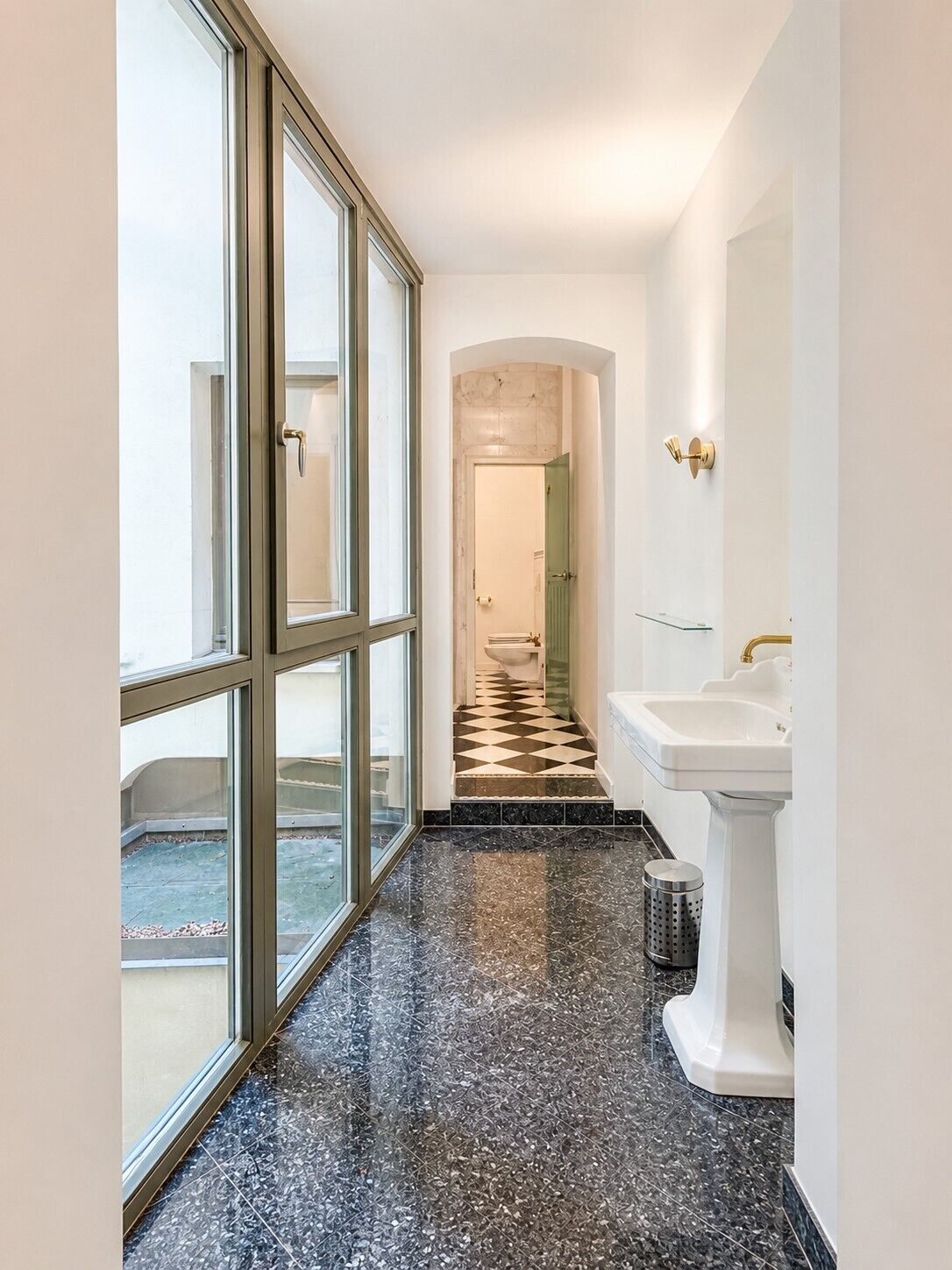 A hallway with a glass door, a white sink, and a checkered floor.
