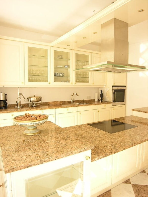 Eine moderne Küche mit weißen Schränken, einer Granit Arbeitsplatte, einem Edelstahlbackofen und einem Schrank mit Glastür.