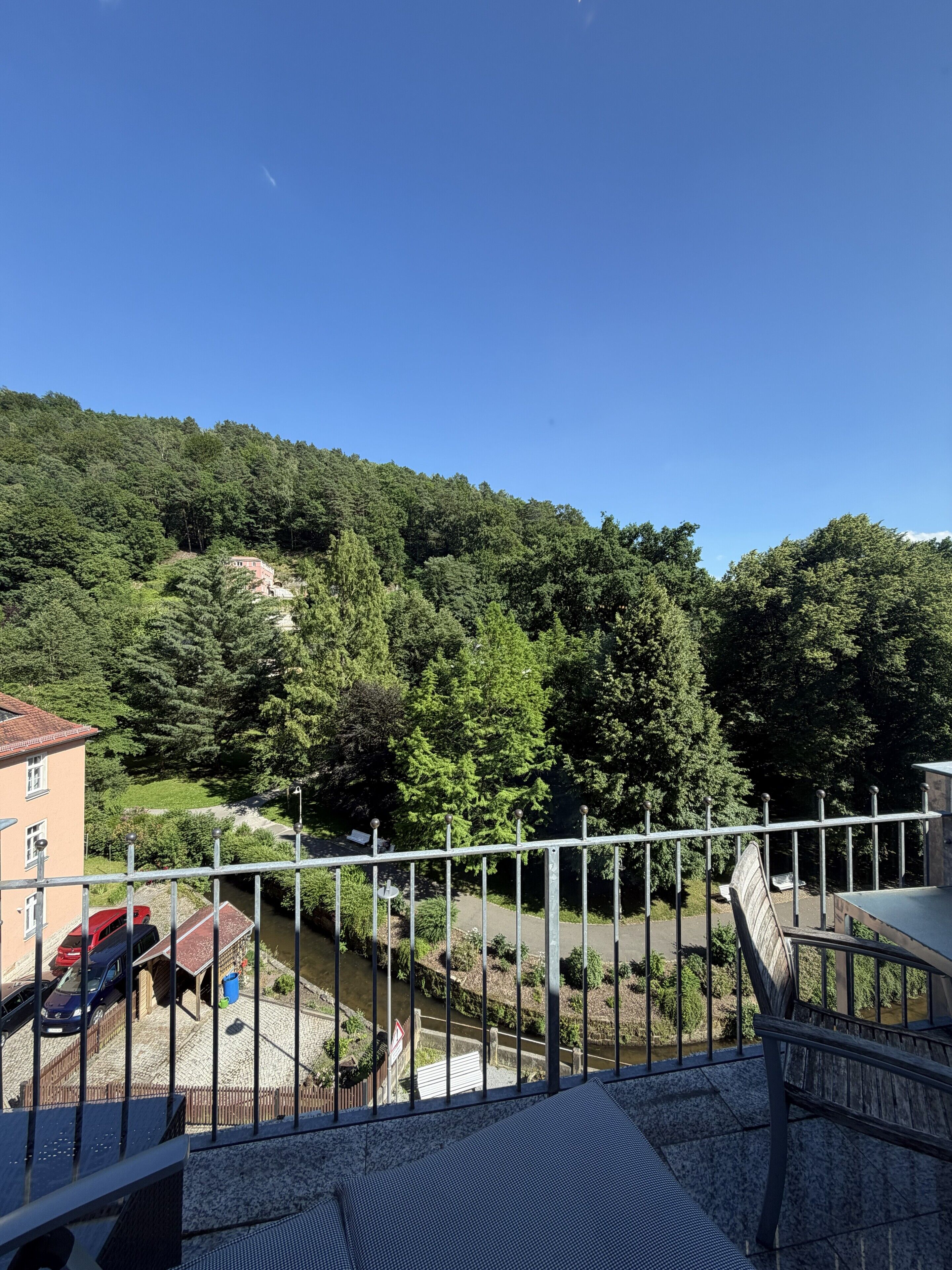A balcony with a view of a river, a red car, and a building with a red roof.