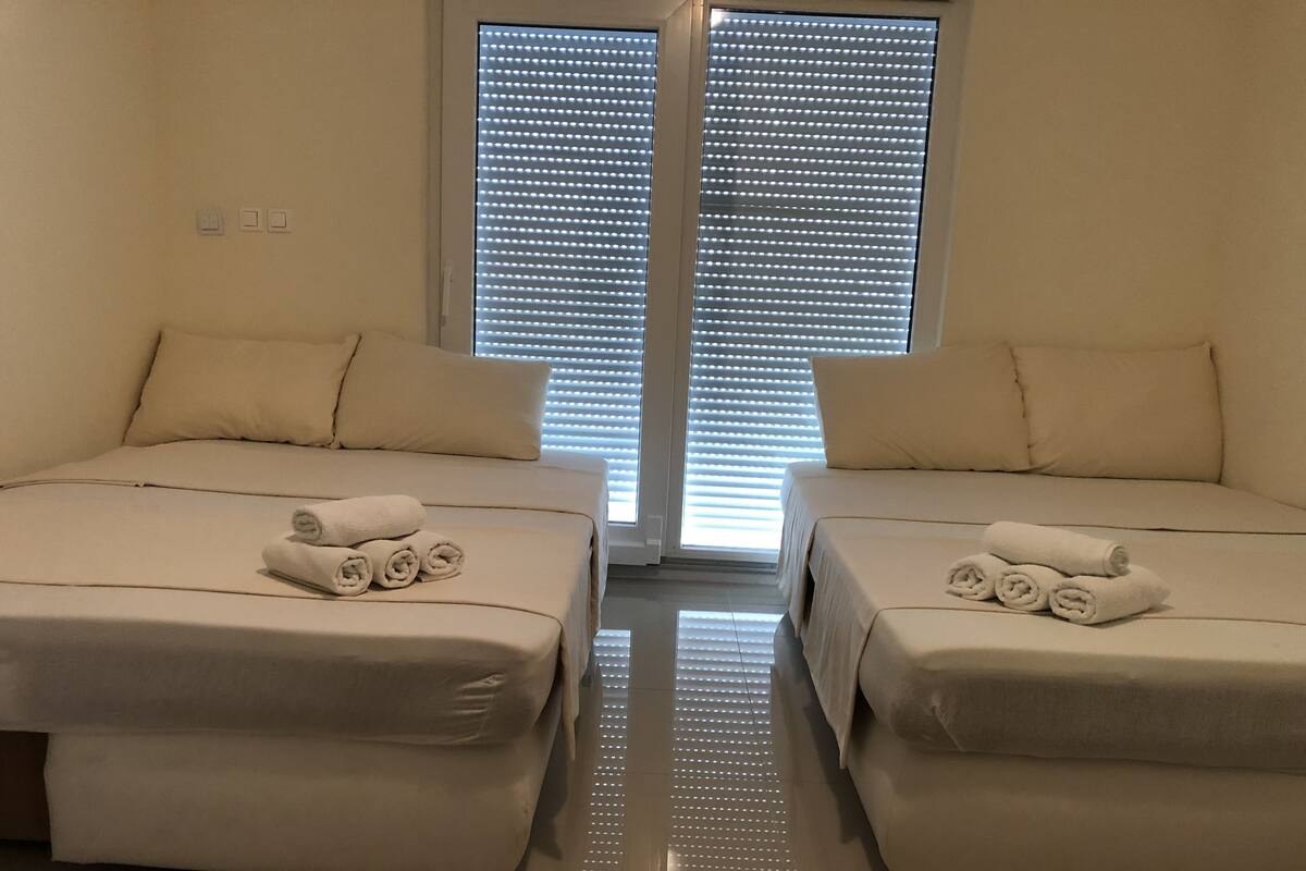A hotel room with two beds, each with a rolled towel on the bed.