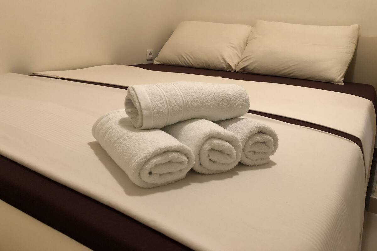 A neatly made bed with white linens and rolled towels.