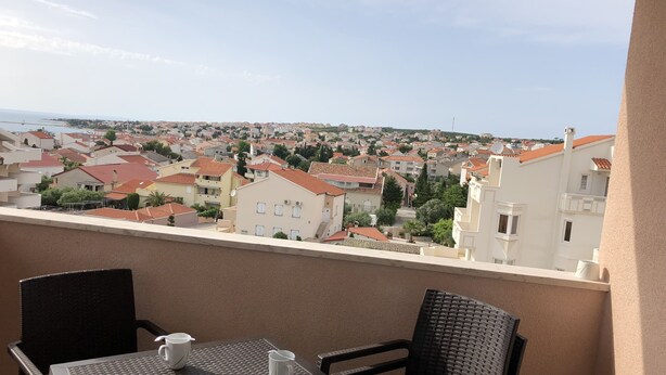A balcony with a table and chairs, overlooking a residential area with red-tiled roofs. - Atrium Novalja (Novalja)