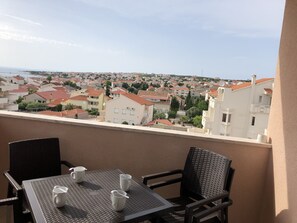 Un balcon avec une table et des chaises, donnant sur un quartier résidentiel aux toits recouverts de tuiles rouges.