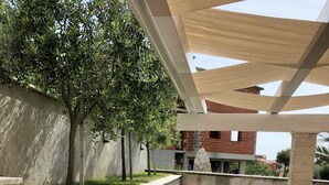 An outdoor patio area with a concrete floor, stone walls, and a pergola structure. - Atrium Novalja (Novalja)